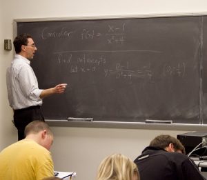 Highland Faculty teaching a complex mathematics equation on a blackboard as students take notes in the foreground