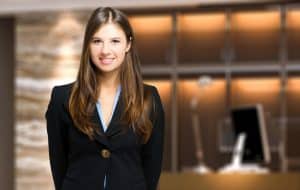 A young woman in a black suit jacket standing outside a building.