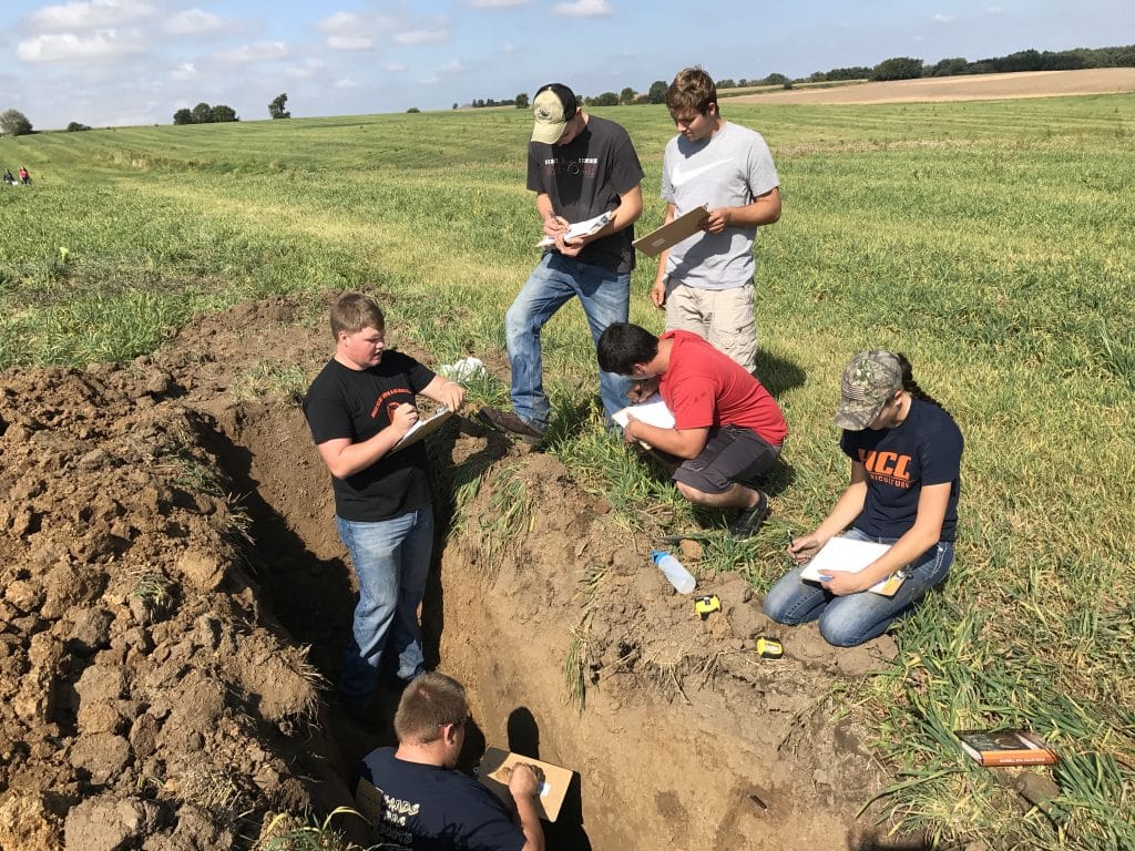 highland students in a crop field taking notes on soil samples