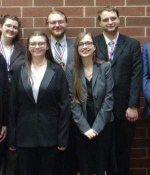 Seven members of the speech and debate team smile for a photo with medals around their necks