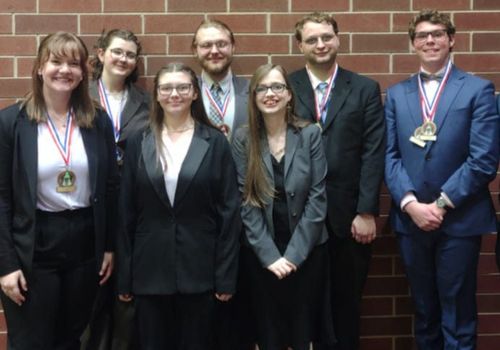 Seven members of the speech and debate team smile for a photo with medals around their necks