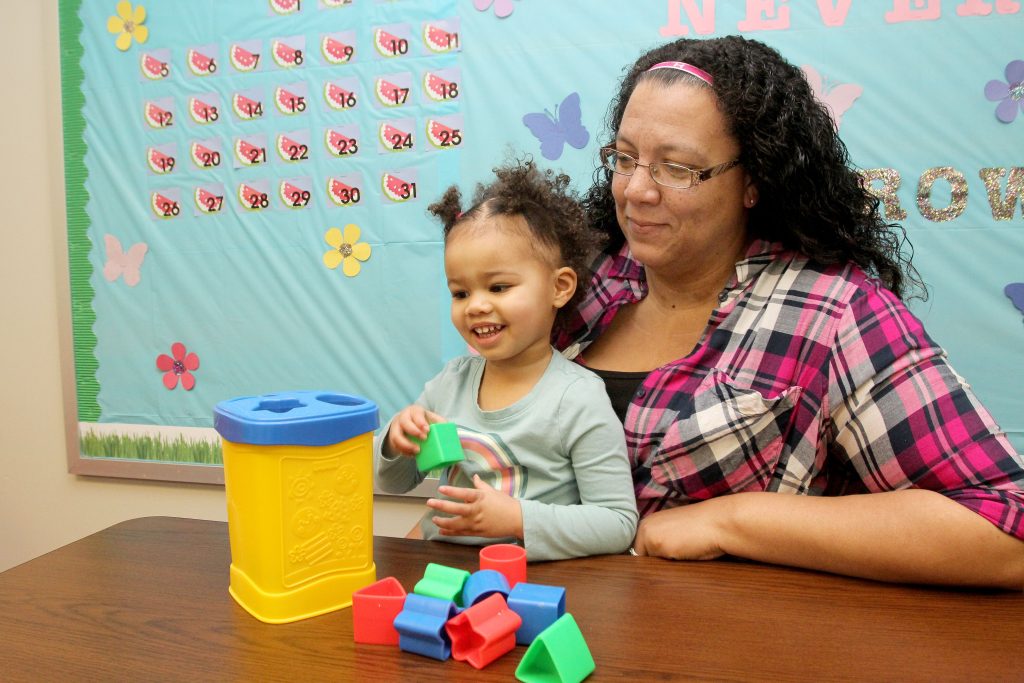 Highland student with a kindergarten student in her lap arranging blocks in a classroom setting