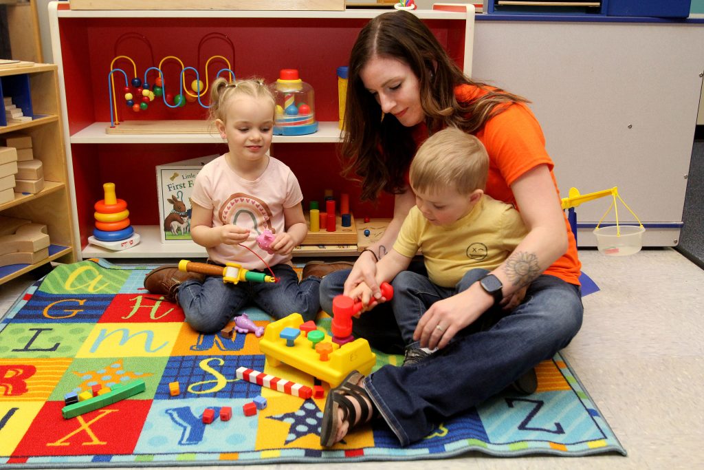 highland student playing with two toddlers in a classroom