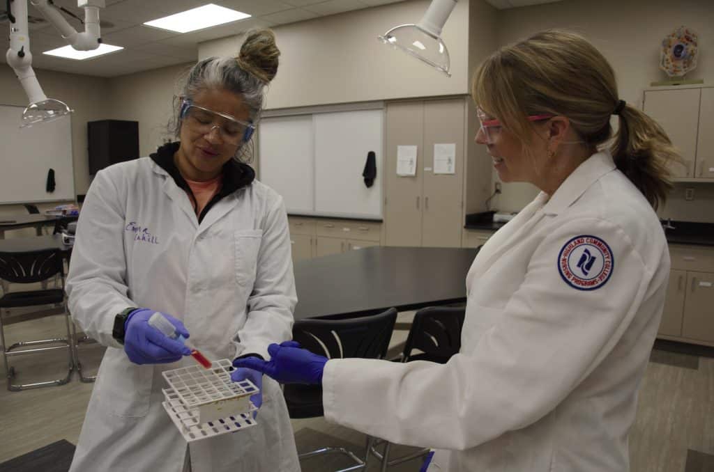 students in lab coats holding lab equipment