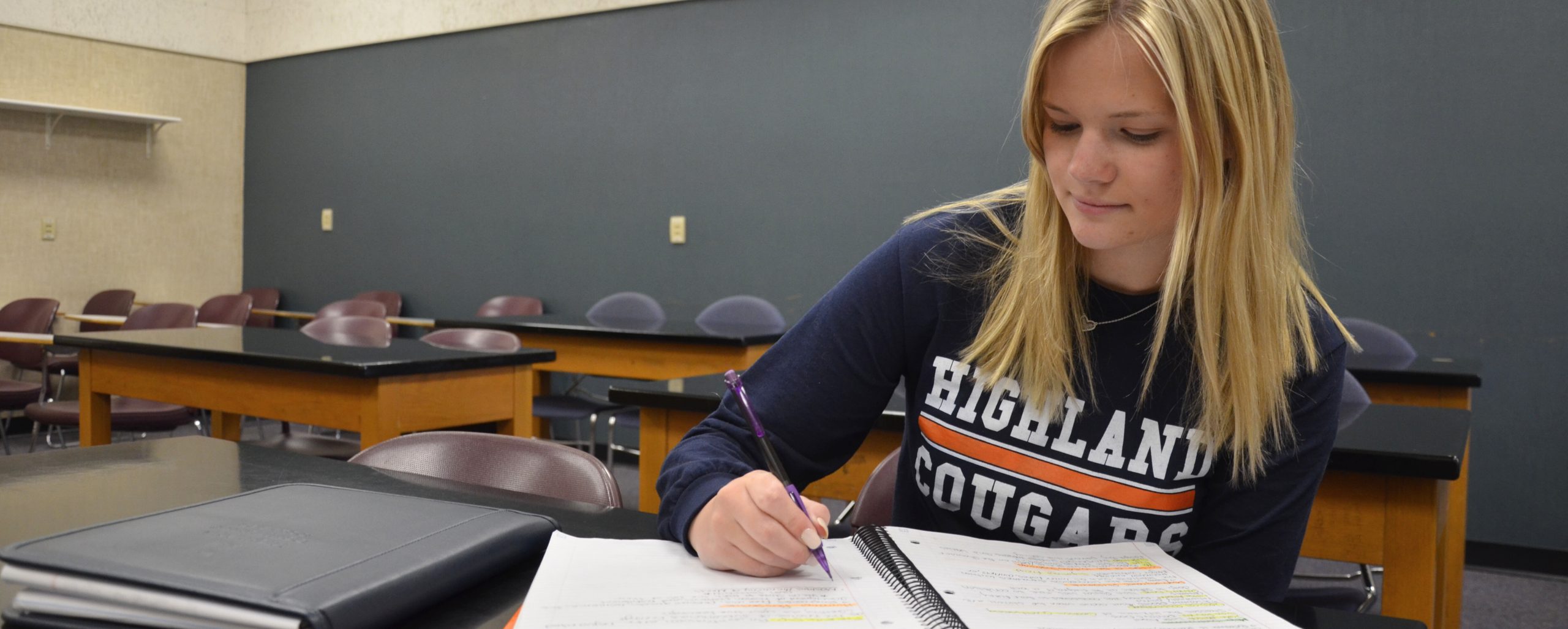 A blond student writing in a notebook in class.