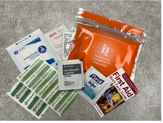 Highland Community College safety kit including bandages, antiseptic wipes, and a small First Aid guide.