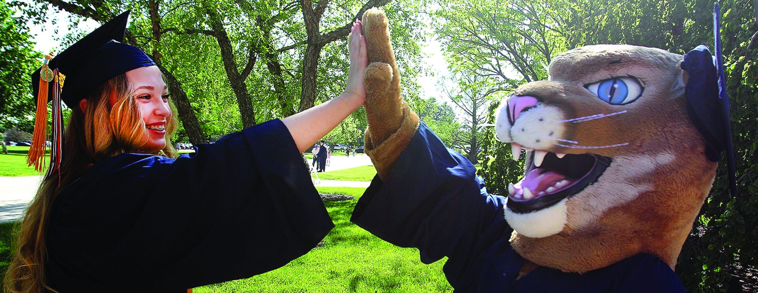 female student in cap and gown "high-five" with Roary mascot