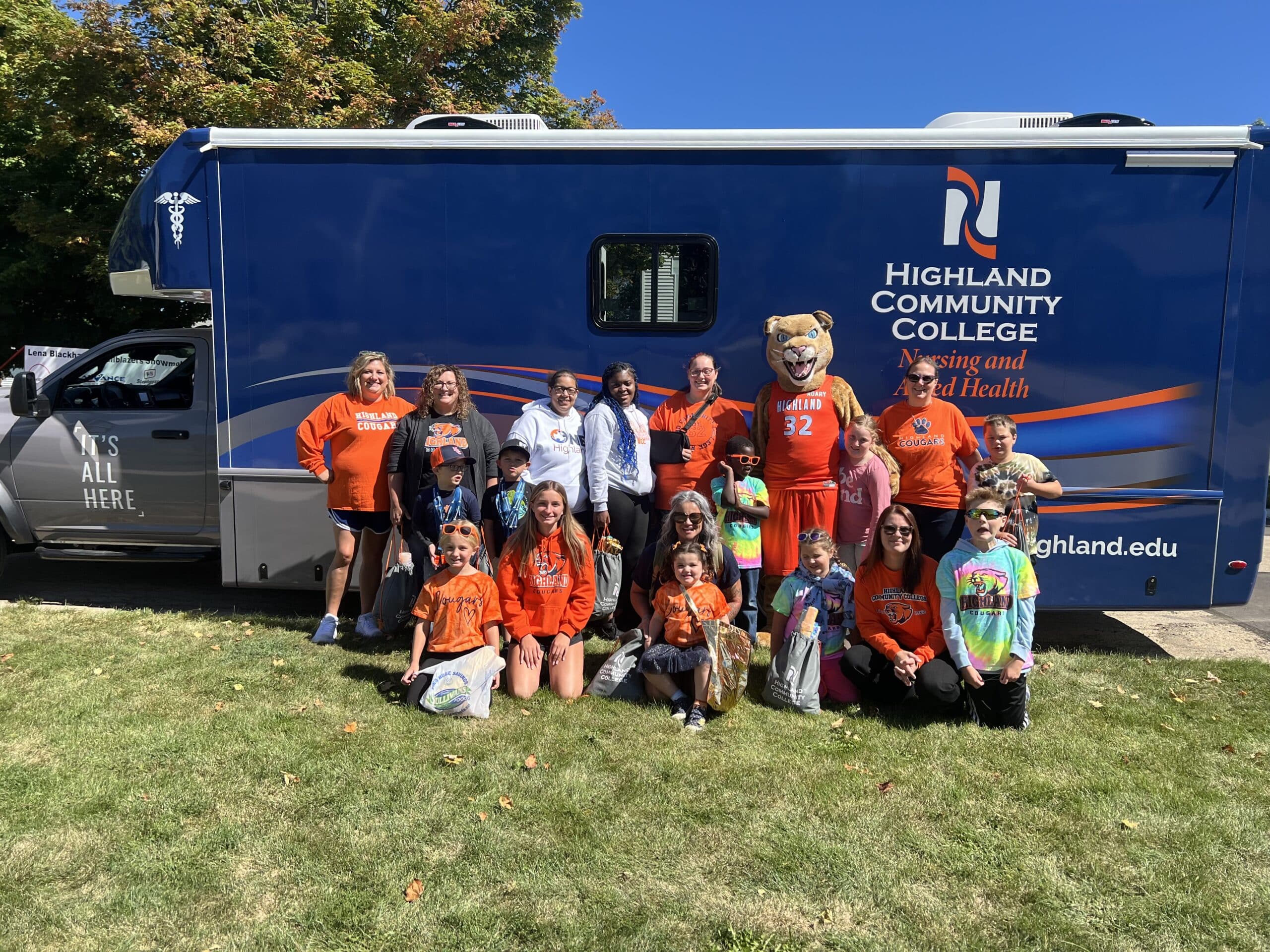 Group of individuals dressed in orange standing in front of blue mobile medical clinic vehicle.
