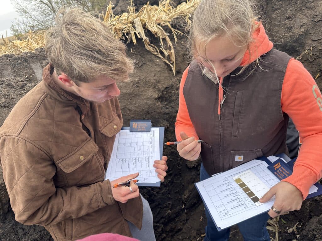 crop and soil science students working in a soil pit taking notes