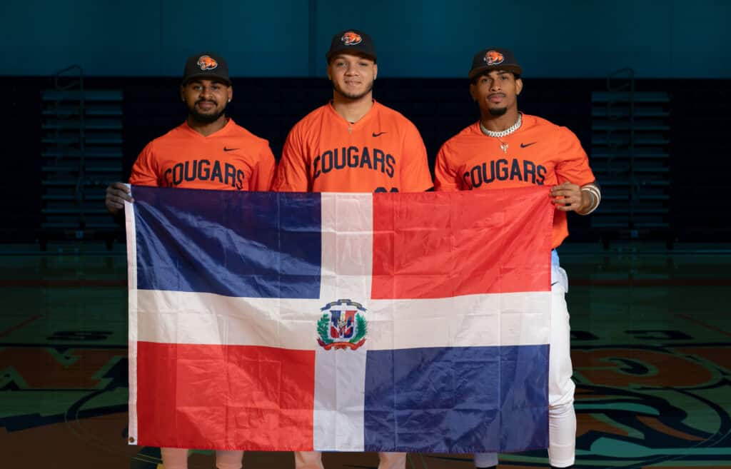 Three international baseball players holding a flag