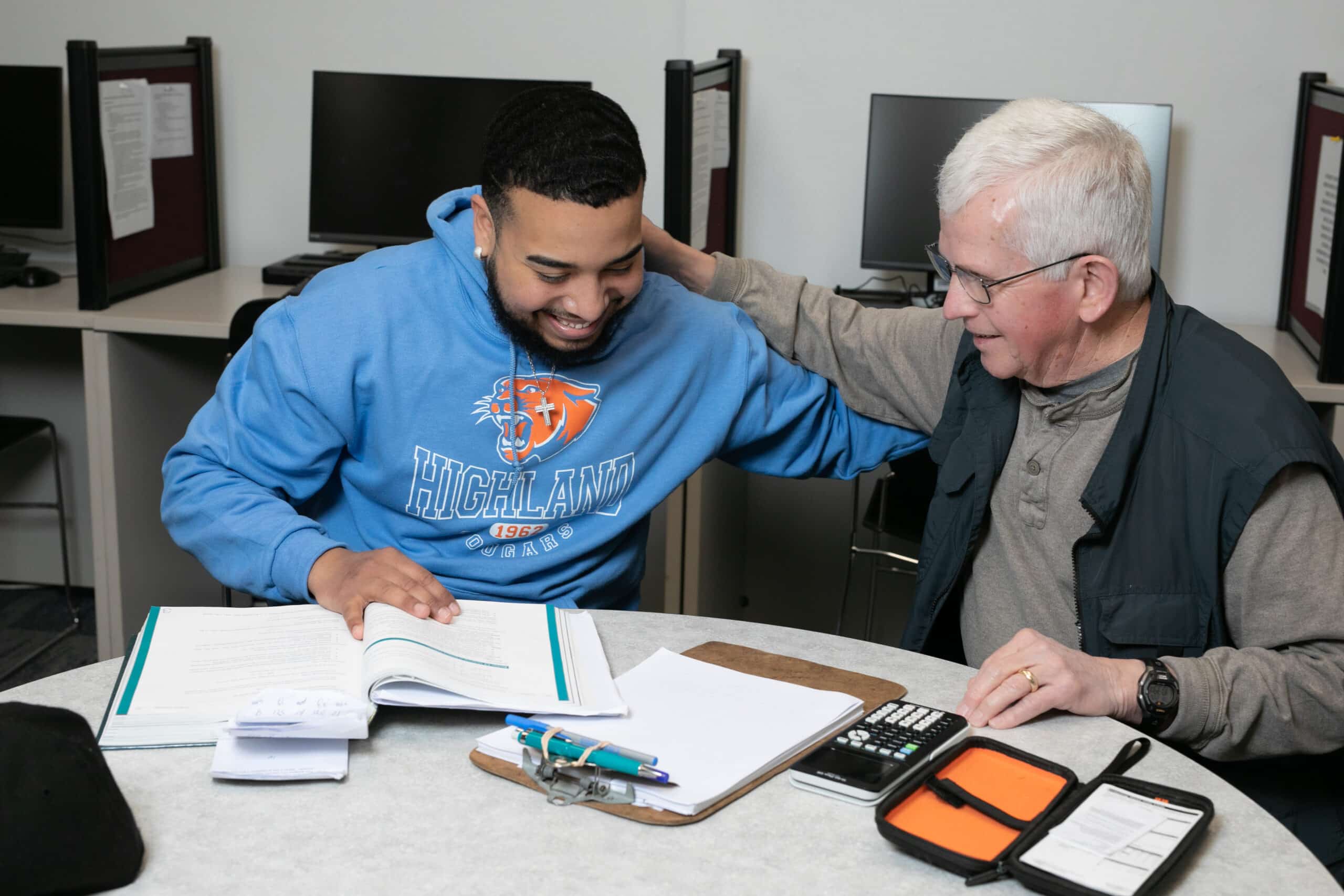 Two people sitting at a table patting each other on the back. One is a student and the other is a tutor.